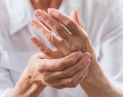 Zwei erwachsene Hände, eine massiert sanft die andere, neutrales unscharfes Hintergrund.