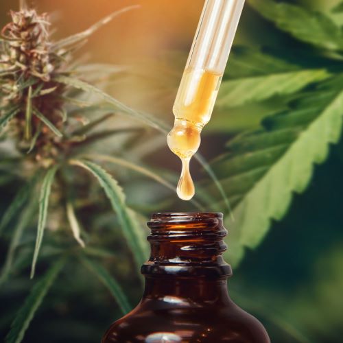 Braune Glasflasche mit Tropfen aus Pipette und grünen Cannabisblättern