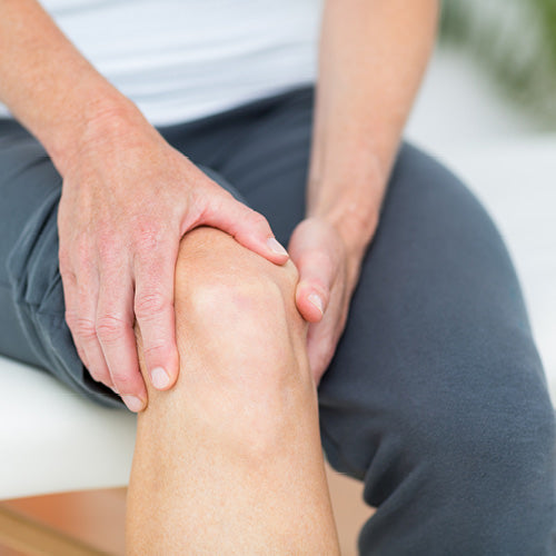 Nahaufnahme von Händen, die ein gebeugtes Knie halten, symbolisiert Gelenkschmerzen.