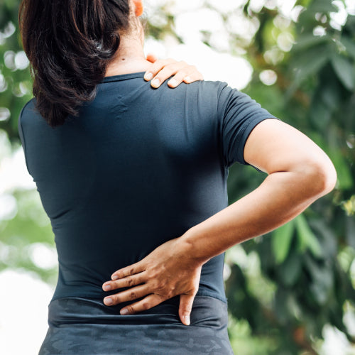 Person im dunklen T-Shirt greift sich an Nacken und unteren Rücken, zeigt Schmerzen